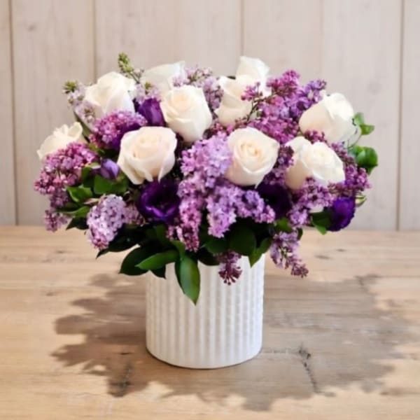 White roses and purple lilacs in a white ribbed vase