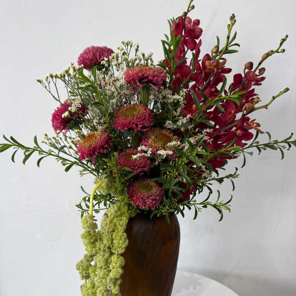 Tall bouquet of magenta flowers and red orchids in a brown vase