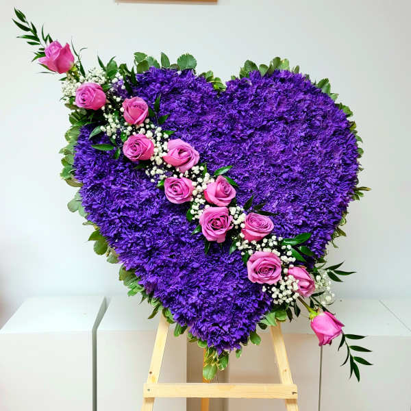 Heart-shaped purple floral arrangement with pink roses on an easel