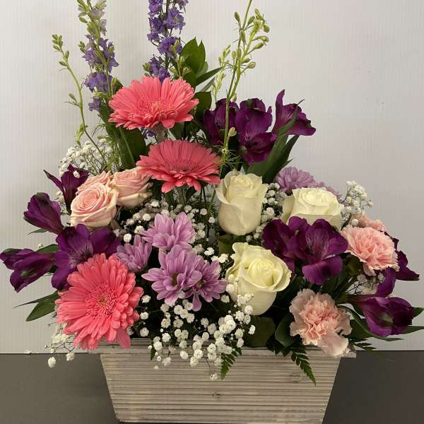 Mixed bouquet in a white rectangular container with pink, purple, and cream flowers