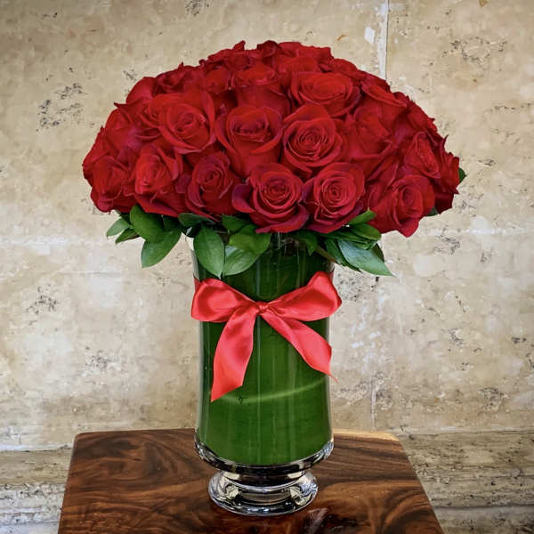 Red roses arranged in a tall glass vase with a red ribbon