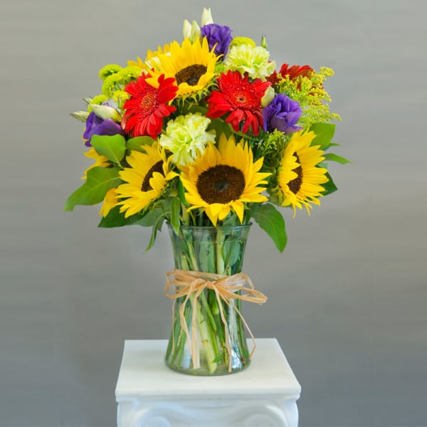 Bouquet of sunflowers, red gerbera daisies, and purple blooms in a glass vase
