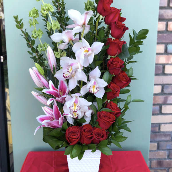 Tall arrangement of red roses, white orchids, and pink lilies in a white vase