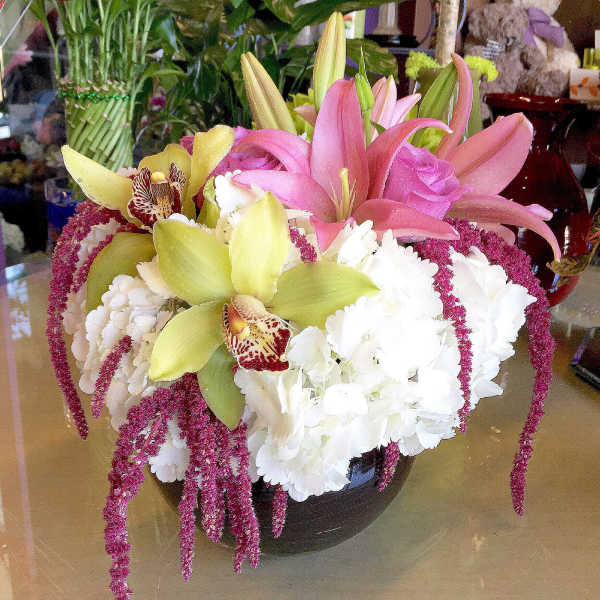 Pink lilies and white hydrangeas in a dark vase with trailing magenta accents