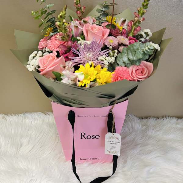 Bouquet of pink roses, yellow daisies, and mixed blooms in pink wrapping