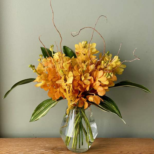 Orange and yellow orchid arrangement in a clear glass vase
