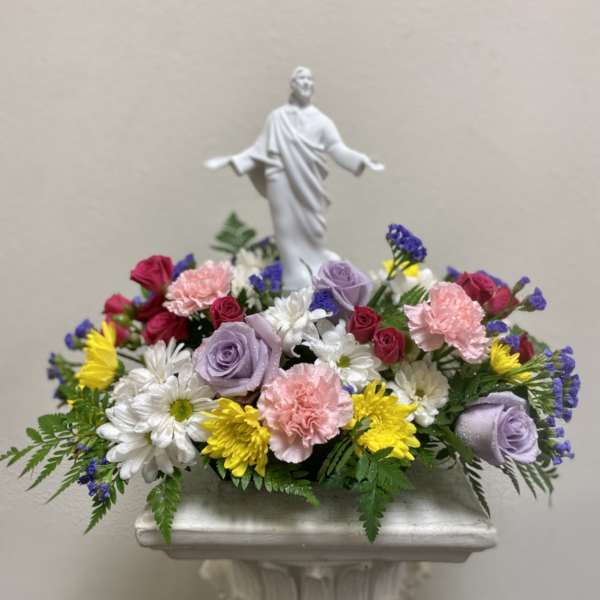 Mixed floral arrangement with a white religious statue centerpiece