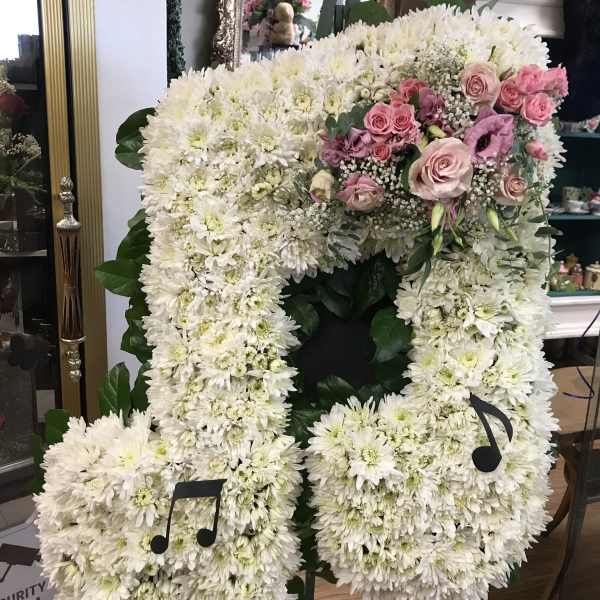 Large white floral standing arrangement with pink roses and music note accents