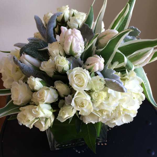 White roses and hydrangeas in a square glass vase with variegated leaves