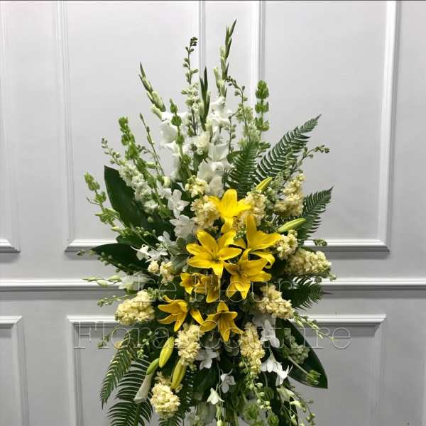 Standing floral spray with yellow lilies and white flowers on an easel