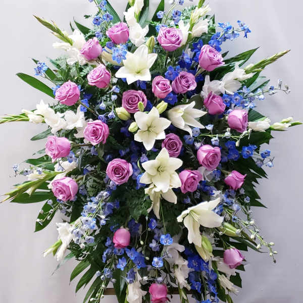 Large standing spray of pink roses, white lilies, and blue flowers