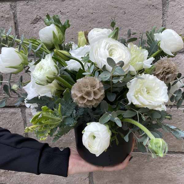 White ranunculus bouquet in a black container with eucalyptus