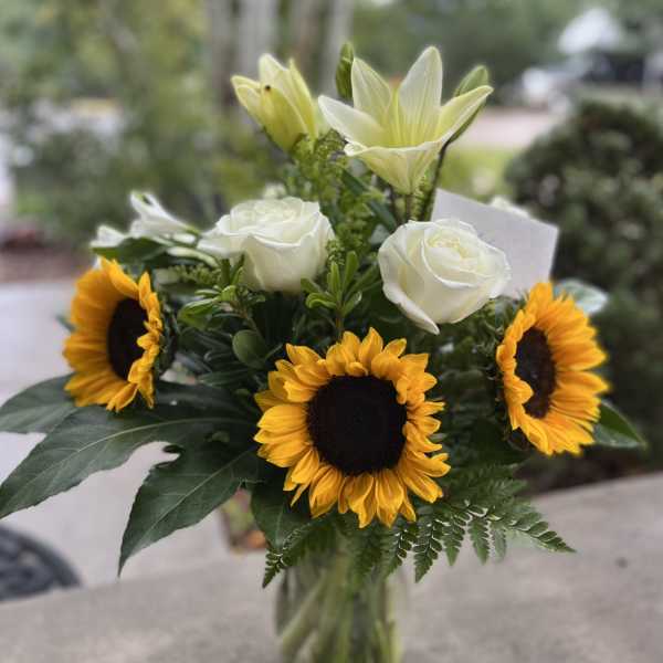Bouquet of sunflowers, white roses, and pale lilies in a glass vase