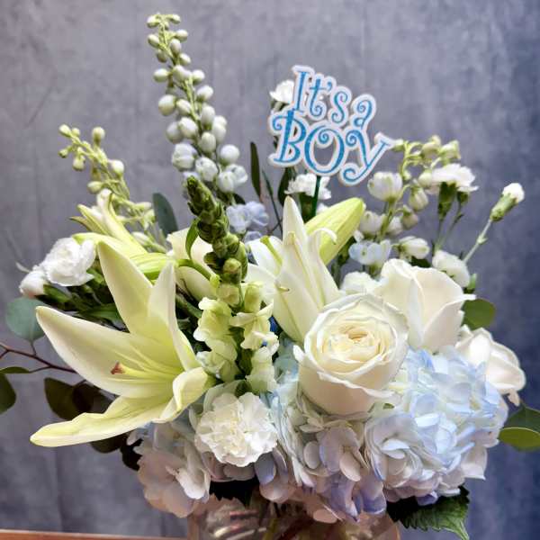 White and pale blue bouquet in a glass vase with an "It's a Boy" sign