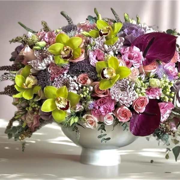 Mixed pink and purple floral arrangement in a white pedestal bowl
