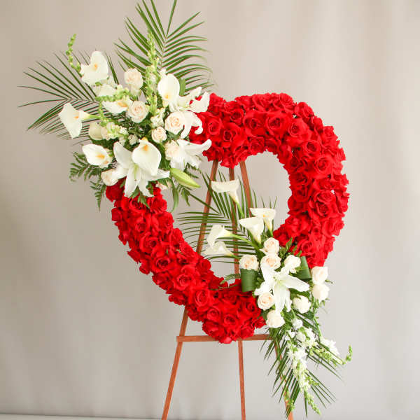 Tall standing heart wreath of red roses with white lilies and calla lilies on a wooden easel.