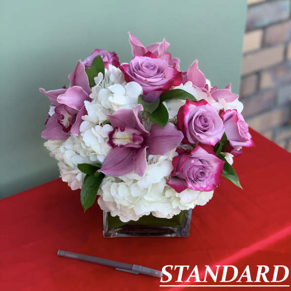 Pink roses and orchids arranged in a square glass vase