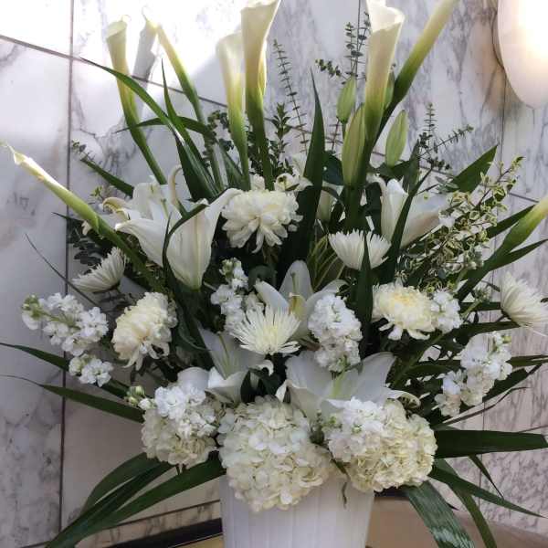 White floral arrangement in a white vase with tall calla lilies and chrysanthemums