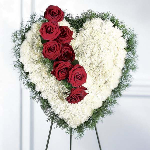 Heart-shaped floral tribute with red roses and white flowers on an easel