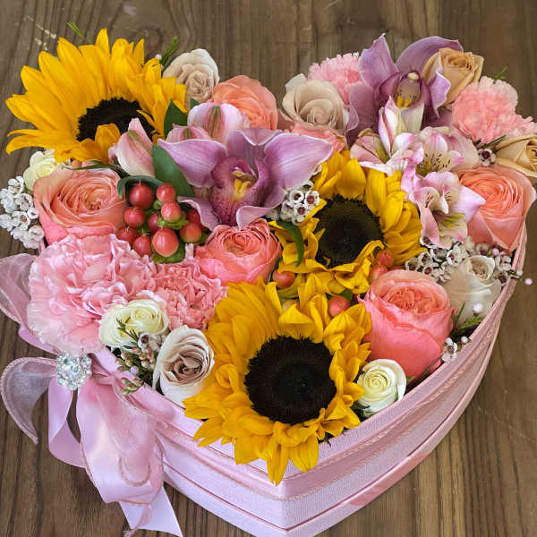 Heart-shaped pink box filled with sunflowers, roses, orchids, and other mixed flowers.