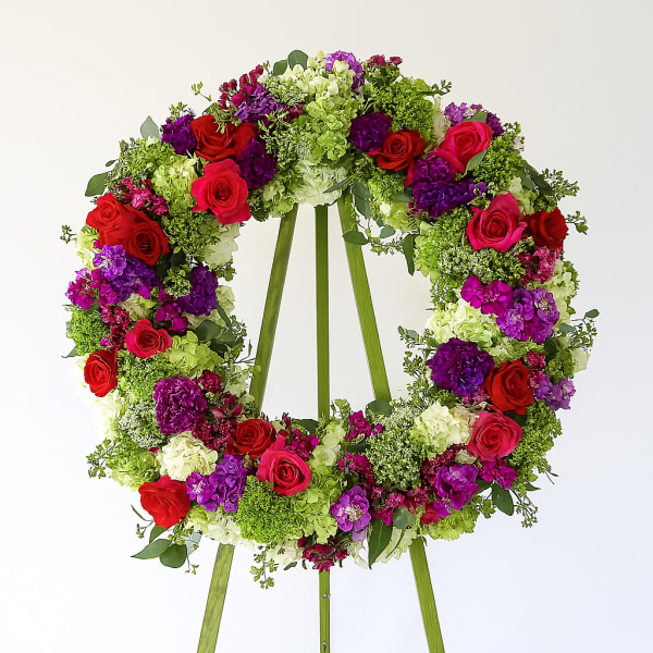 Large floral wreath on a stand with red, pink, purple, and green blooms