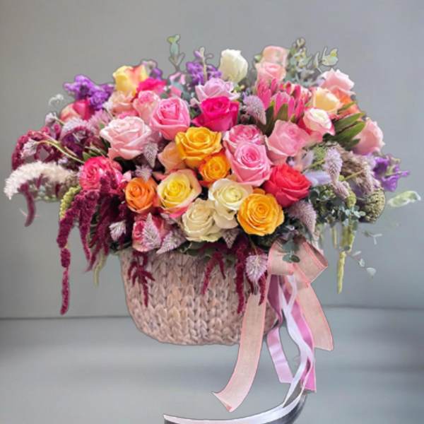 Mixed bouquet of colorful roses in a woven basket with ribbon