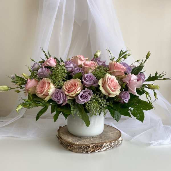 Pink and lavender roses arranged in a white vase