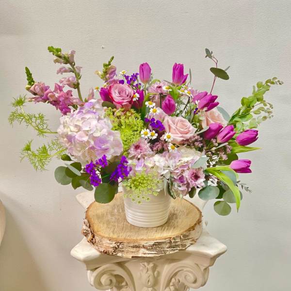 Mixed pink and purple flowers in a white vase on a wood slice
