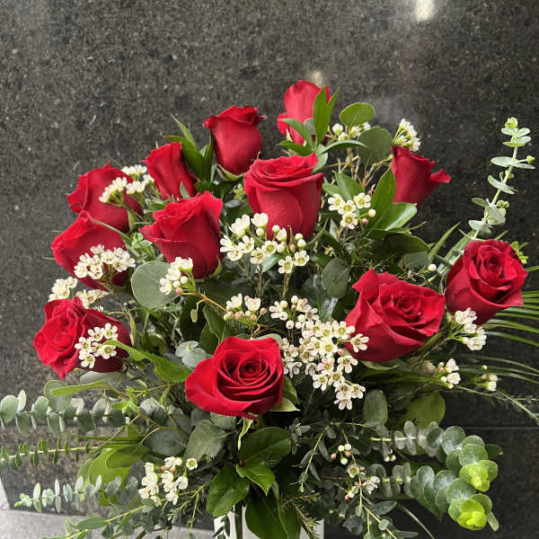 Red roses arranged in a white vase with white filler flowers and greenery