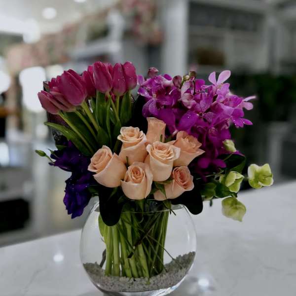 Bouquet of peach roses, purple tulips, and magenta orchids in a glass vase