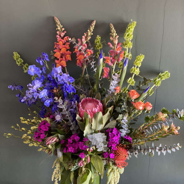 Tall mixed flower arrangement in a green vase with bright pink, blue, and orange blooms