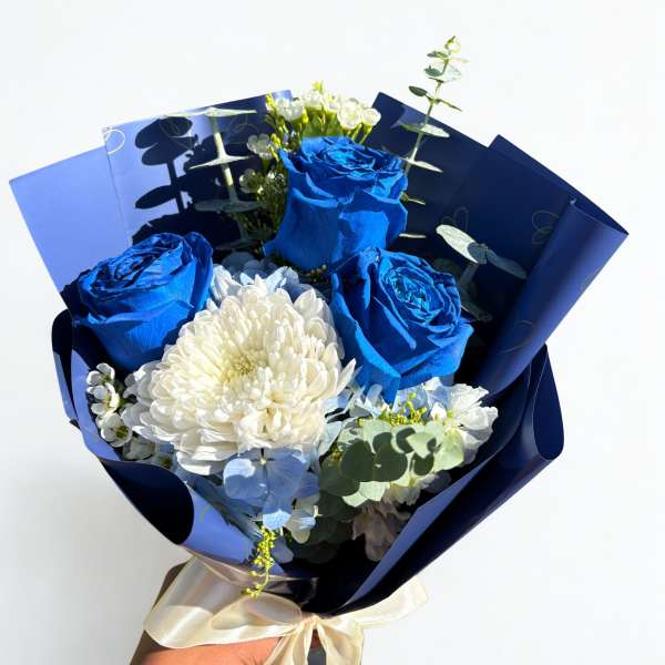 Bouquet of blue roses and white flowers wrapped in dark blue paper