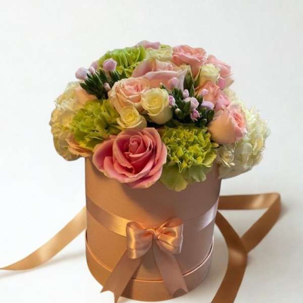 Pink and cream roses arranged in a round hatbox with satin ribbon