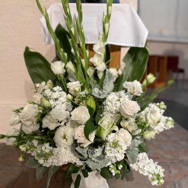 White floral arrangement in a white pedestal vase with tall green stems