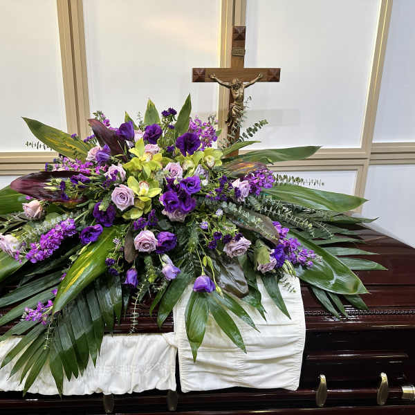 Purple and green floral casket spray with a crucifix behind it