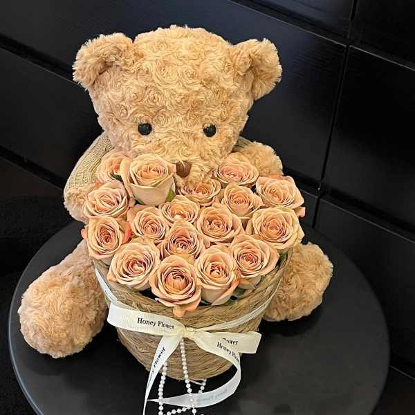 Teddy bear holding a heart-shaped box of peach roses