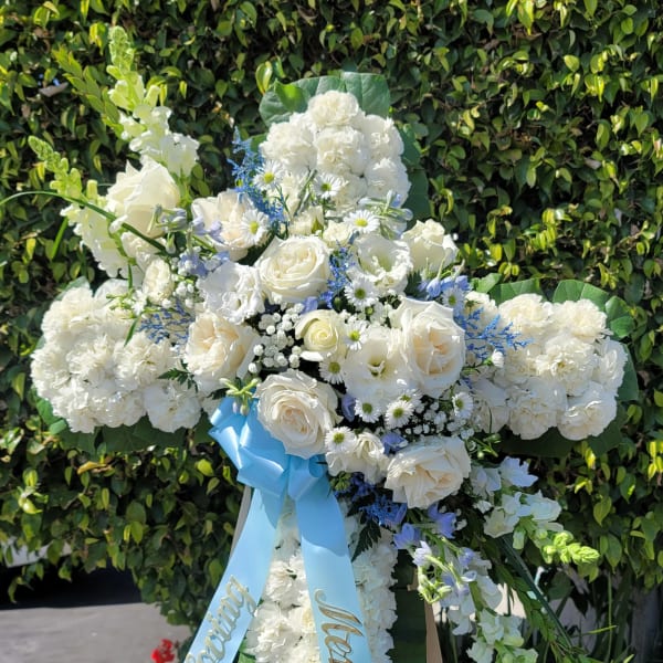 White floral standing cross on an easel with a blue ribbon