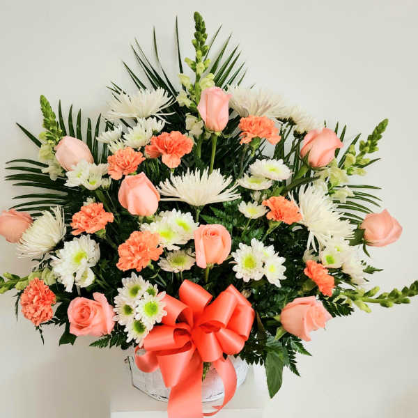 Pink roses and white-orange mixed flowers in a white basket with a coral bow