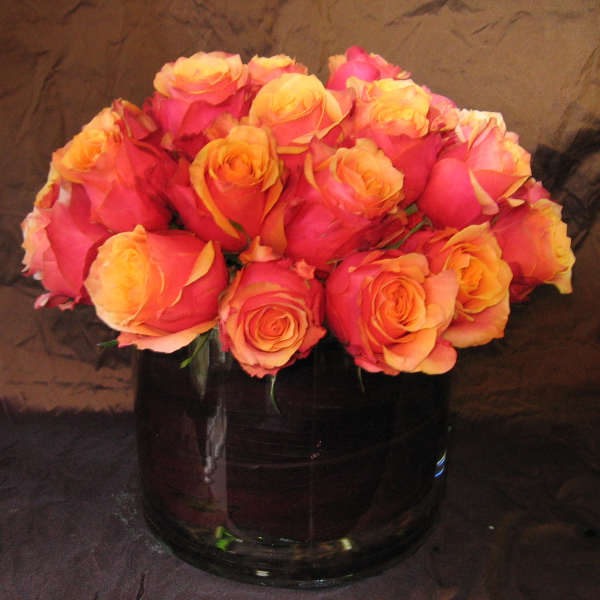 Pink and orange roses arranged in a dark glass vase