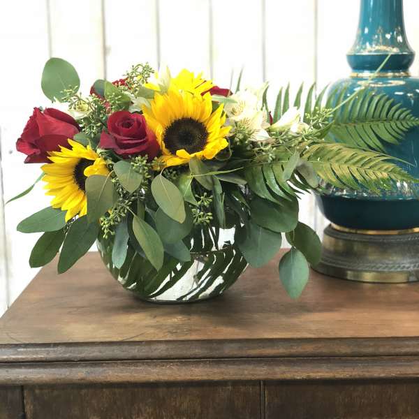 Bouquet of red roses and sunflowers in a low glass vase