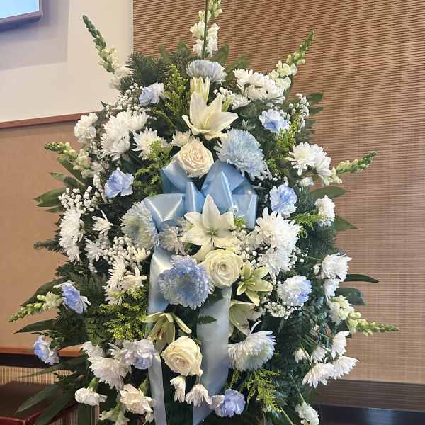 Large white and pale blue funeral spray on an easel