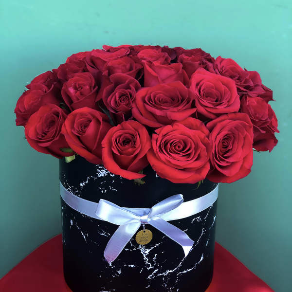 Red roses arranged in a black round box with a white ribbon