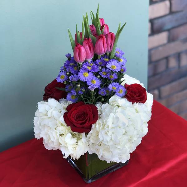 Bouquet of red roses, white hydrangeas, purple daisies, and pink tulips in a glass vase