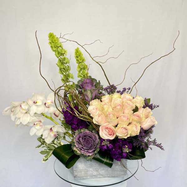 Arrangement of pale pink roses, white orchids, and purple flowers in a silver box