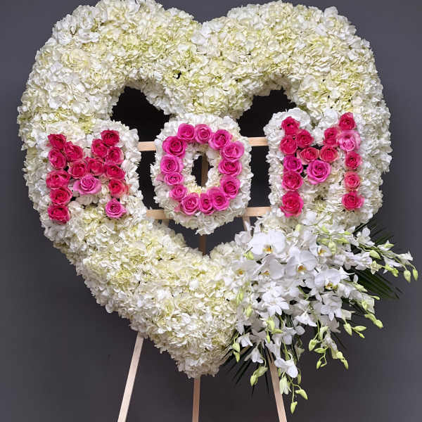 Heart-shaped floral tribute with white hydrangeas, pink roses, and white orchids on an easel