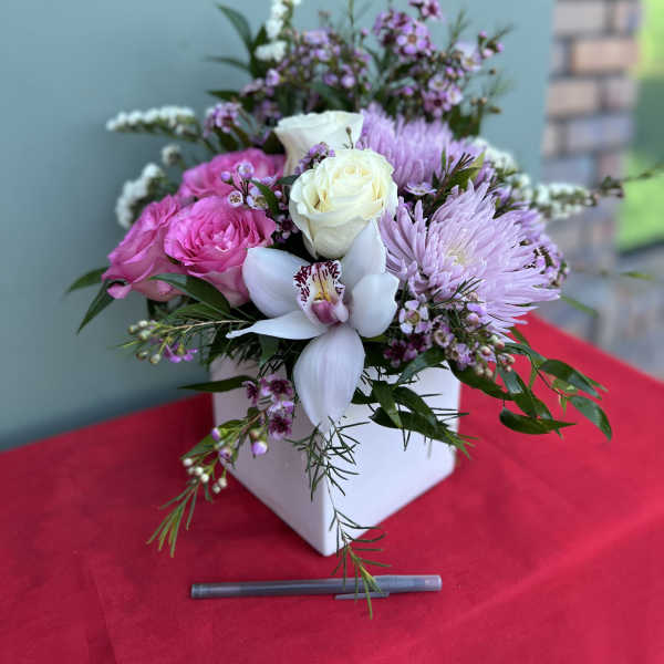 Pink and white floral arrangement in a white box with an orchid