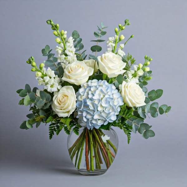 White roses and a blue hydrangea bouquet in a clear glass vase