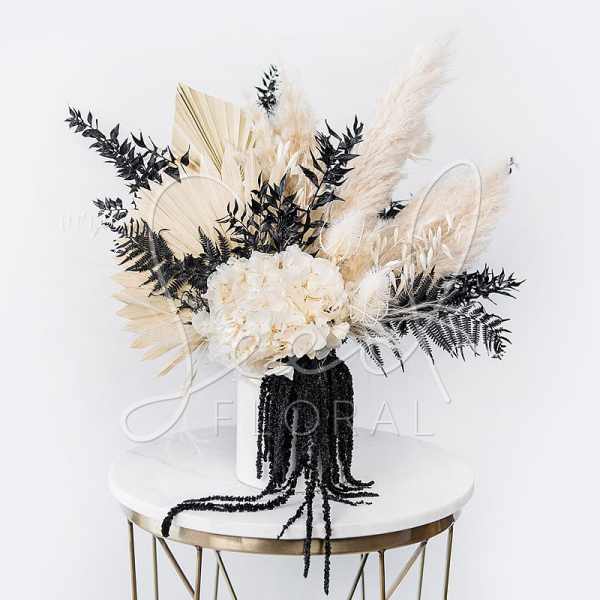 White floral arrangement with black and beige dried accents in a black vase