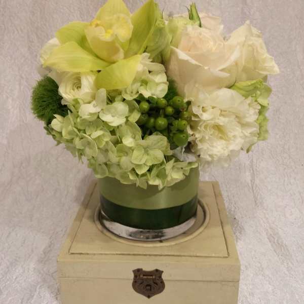 Green and white floral arrangement in a round box on a wooden base