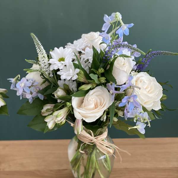 White roses and blue flowers arranged in a glass vase